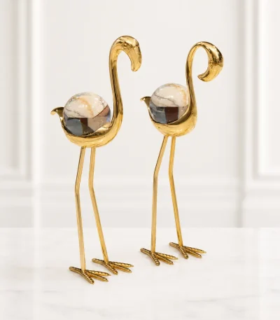 Set of two elegant gold flamingo figurines with clear crystal spheres as their bodies, standing on a speckled marble tabletop