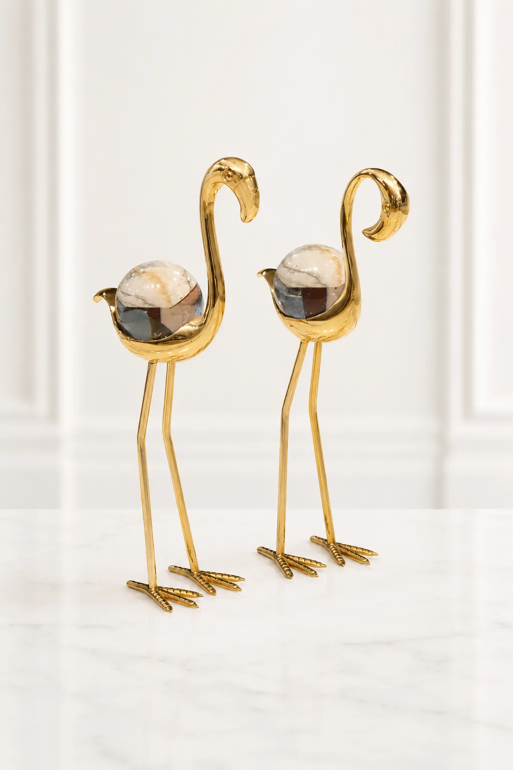 Modern Metal Bird Figurines for Living Room, Office, and Home Decor Set of two elegant gold flamingo figurines with clear crystal spheres as their bodies, standing on a speckled marble tabletop