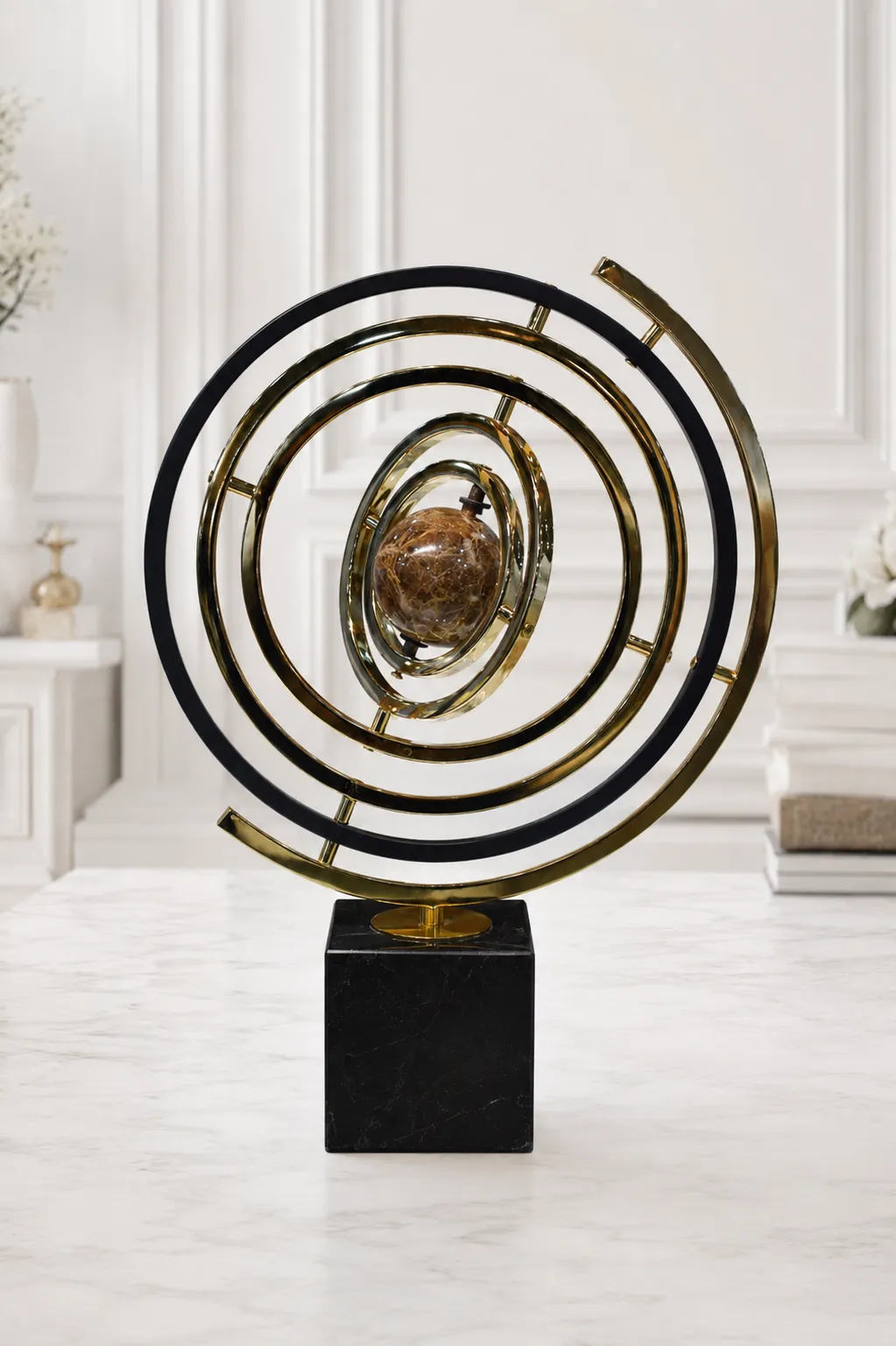 Modern Gold & Black Astrolabe Kinetic-Style Tabletop Sculpture A modern kinetic-style armillary sphere sculpture featuring concentric gold and black metal rings surrounding a brown marbled central orb, standing on a black square base on a light marble tabletop