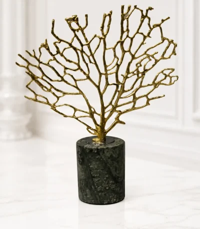 A luxury tabletop sculpture featuring an intricate gold metal coral branch structure mounted on a dark green marbled cylindrical stone base, sitting on a light marble table