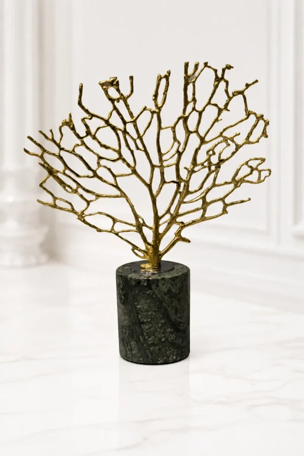 A luxury tabletop sculpture featuring an intricate gold metal coral branch structure mounted on a dark green marbled cylindrical stone base, sitting on a light marble table