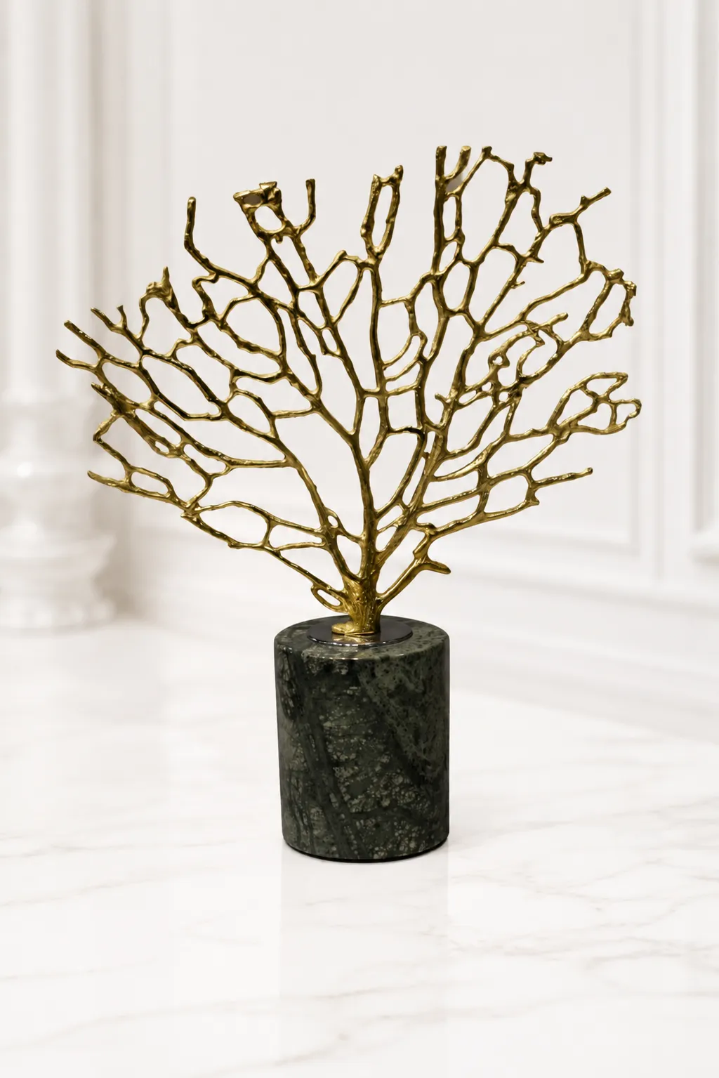 Decorative Golden Coral Tree Accent A luxury tabletop sculpture featuring an intricate gold metal coral branch structure mounted on a dark green marbled cylindrical stone base, sitting on a light marble table