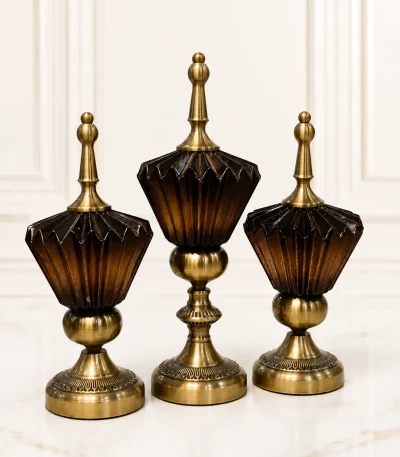 A set of three vintage-style decorative jars of varying heights featuring fluted dark brown glass containers mounted on antique brass pedestal bases with matching pointed brass finial lids, sitting on a speckled marble tabletop