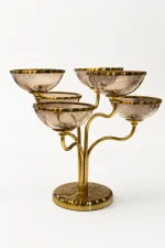 A modern five-cup candelabra featuring a branching brushed-gold metal frame supporting shallow, translucent purple glass bowls with gold rims, sitting on a light marble tabletop