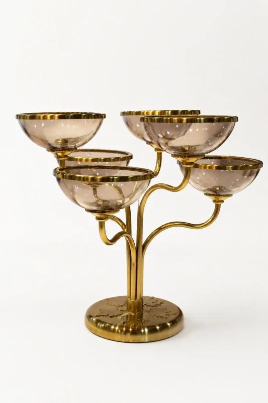 A modern five-cup candelabra featuring a branching brushed-gold metal frame supporting shallow, translucent purple glass bowls with gold rims, sitting on a light marble tabletop