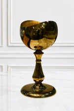 A luxury goblet-style tabletop chalice made of highly polished gold metal with a mirror-like finish and a wavy rim, standing on an ornate pedestal stem and wide circular base on a light speckled marble surface