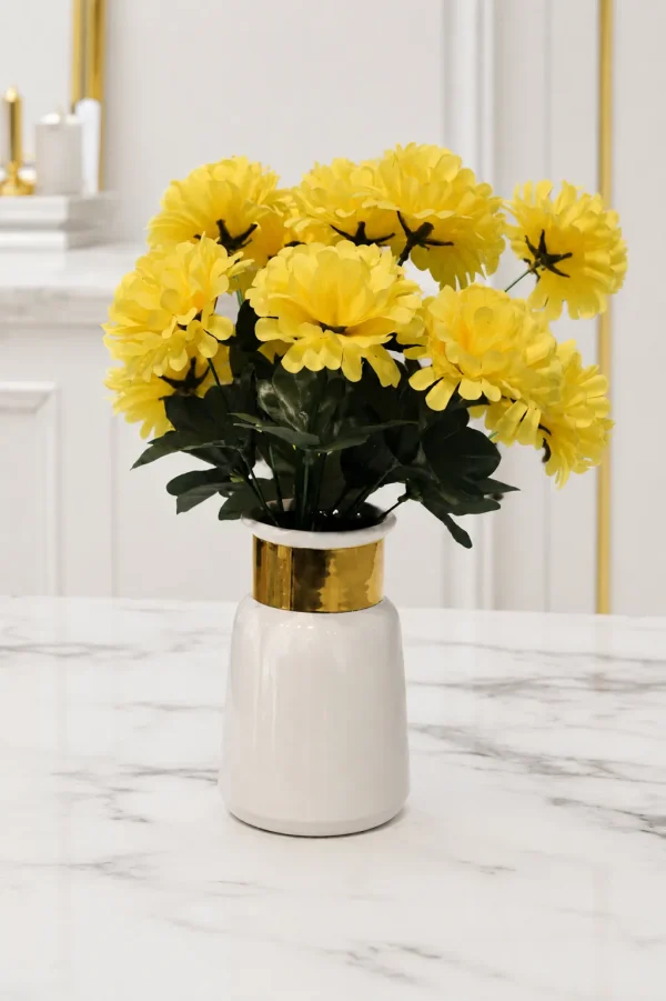 A modern white ceramic vase with a glossy finish and a thick polished gold band around its neck, holding a bouquet of faux yellow flowers on a light marble table