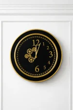 Black and gold luxury wall clock with decorative gear design and modern round frame mounted on a marble-textured wall.