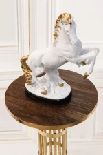 A majestic decorative statue of a white horse with a textured gold mane, tail, and hooves rearing on its hind legs, displayed on a round wood-grain accent table