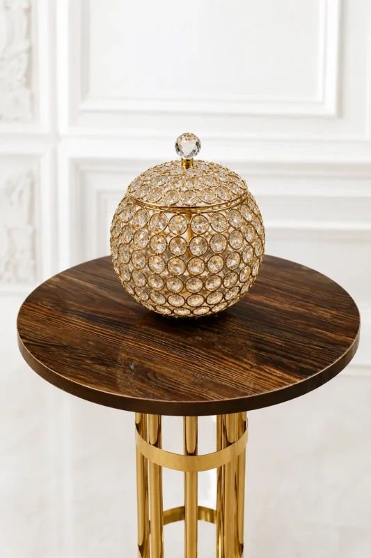 A luxury spherical decorative jar crafted from a gold-plated metal wire lattice woven with multifaceted clear crystal beads, complete with a matching lidded top and crystal finial knob, sitting on a round wood-grain pedestal table