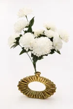 A contemporary metallic gold ceramic vase with a hollow oval doughnut shape and a deep, radiating ribbed texture, holding a full bouquet of white faux flowers on a round dark wood side table