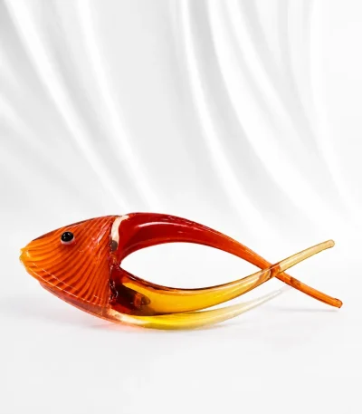 Handcrafted amber glass fish figurine with a translucent golden tail displayed on a marble table.