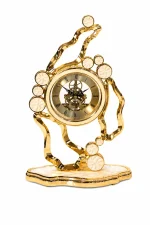 Luxury gold metal table clock with a decorative bird perched on a branch, featuring a skeleton dial, Roman numerals, and a crystal-studded bezel.