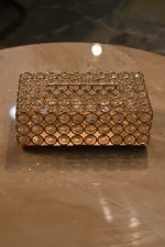A luxury rectangular tissue box cover crafted from a gold-plated metal wire lattice woven with multifaceted clear crystal beads, featuring a central top slot for dispensing tissues, sitting on a polished beige marble surface
