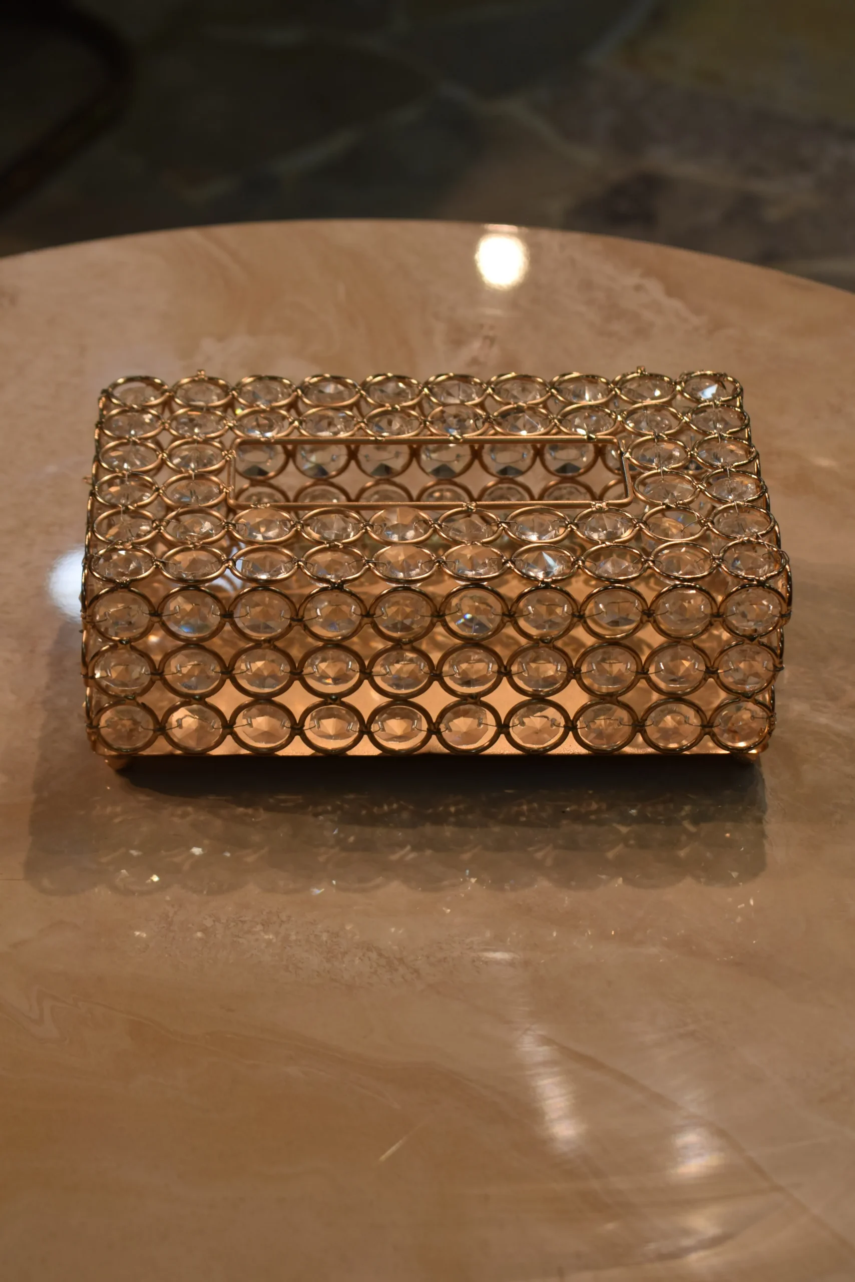 Ornate Crystal-Beaded Rectangular Tissue Organizer Case A luxury rectangular tissue box cover crafted from a gold-plated metal wire lattice woven with multifaceted clear crystal beads, featuring a central top slot for dispensing tissues, sitting on a polished beige marble surface