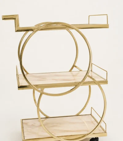 Glamorous geometric gold 3-tier bar cart showcasing an intersecting double circle frame, beige faux-marble shelves, and black rolling caster wheels over a clean white background.