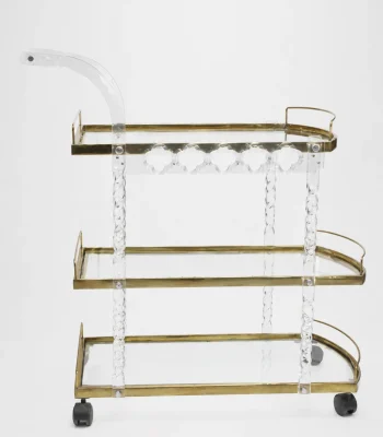 Premium clear acrylic and gold 3-tier bar cart featuring twisted lucite support pillars, transparent glass shelves, an integrated curved handle, and rolling caster wheels over a solid white backdrop.