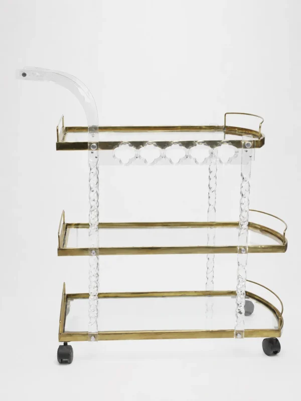 Premium clear acrylic and gold 3-tier bar cart featuring twisted lucite support pillars, transparent glass shelves, an integrated curved handle, and rolling caster wheels over a solid white backdrop.