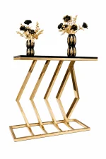 A luxury rectangular console table with a polished gold metal base featuring an abstract parallel chevron and diamond design, topped with a smooth black surface displaying two black and gold decorative vases.