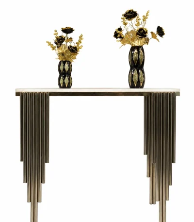 A modern luxury console table with a polished white marble top and a unique pedestal base made from clustered, stepped vertical metal pipes, styled with two black and gold decorative vases against a solid white background.