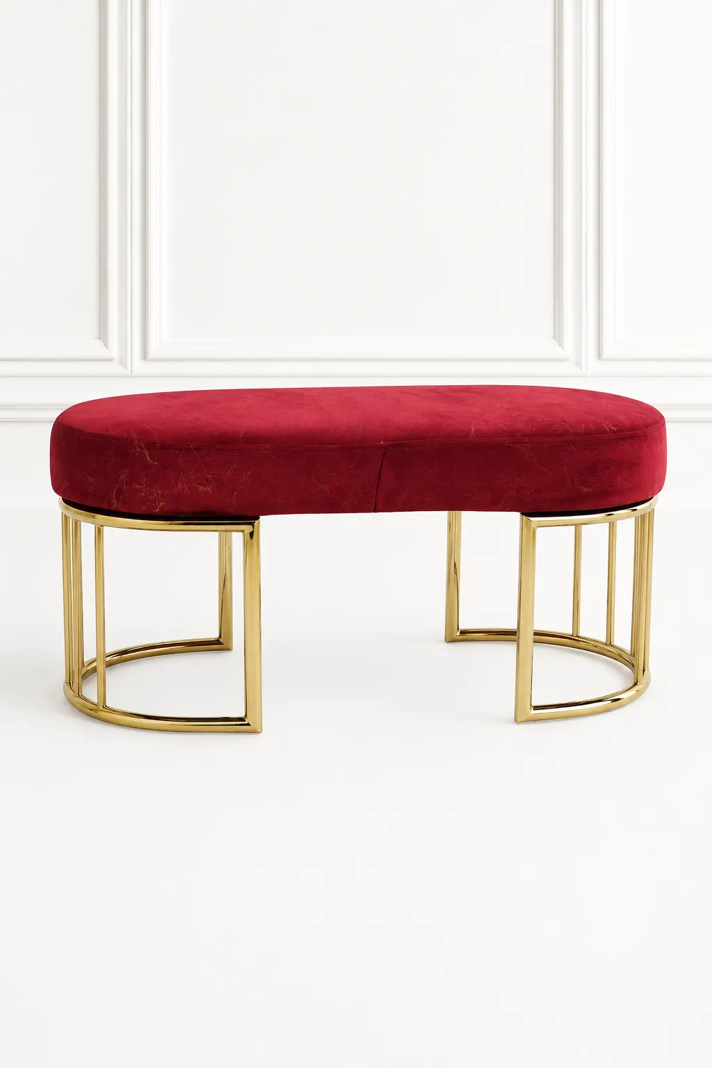 Red Velvet Gold Bench – Modern Oval Upholstered Entryway Accent Ottoman Luxury red velvet gold bench from featuring an oval upholstered crimson seat and polished, semi-circular geometric cage legs against a white wall.