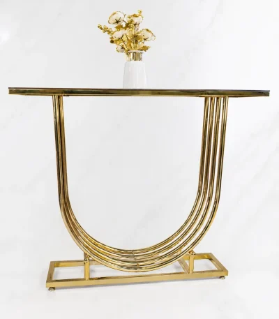 Modern gold U shaped console table from featuring a multi-layered curved base, dark glass top, and a white vase with golden flowers.