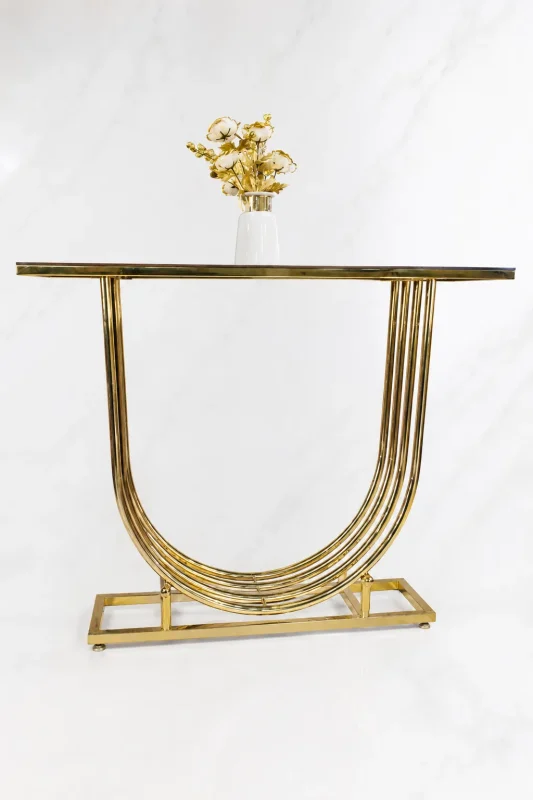Modern gold U shaped console table from featuring a multi-layered curved base, dark glass top, and a white vase with golden flowers.