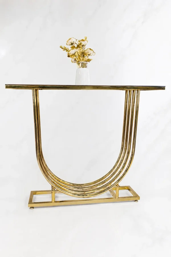 Modern gold U shaped console table from featuring a multi-layered curved base, dark glass top, and a white vase with golden flowers.