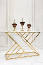 Luxury modern console table featuring a white faux-marble top and a polished gold geometric metal frame, displayed against a white paneled wall.