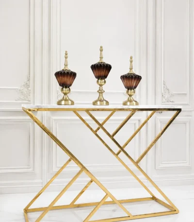 Luxury modern console table featuring a white faux-marble top and a polished gold geometric metal frame, displayed against a white paneled wall.