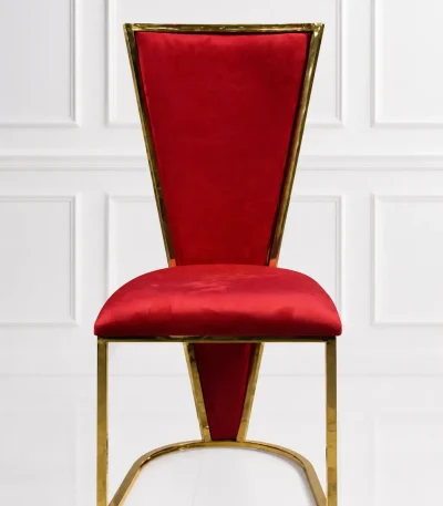 Luxury high-back dining chair featuring royal red velvet upholstery and a polished gold metallic trim frame against a white paneled wall background.
