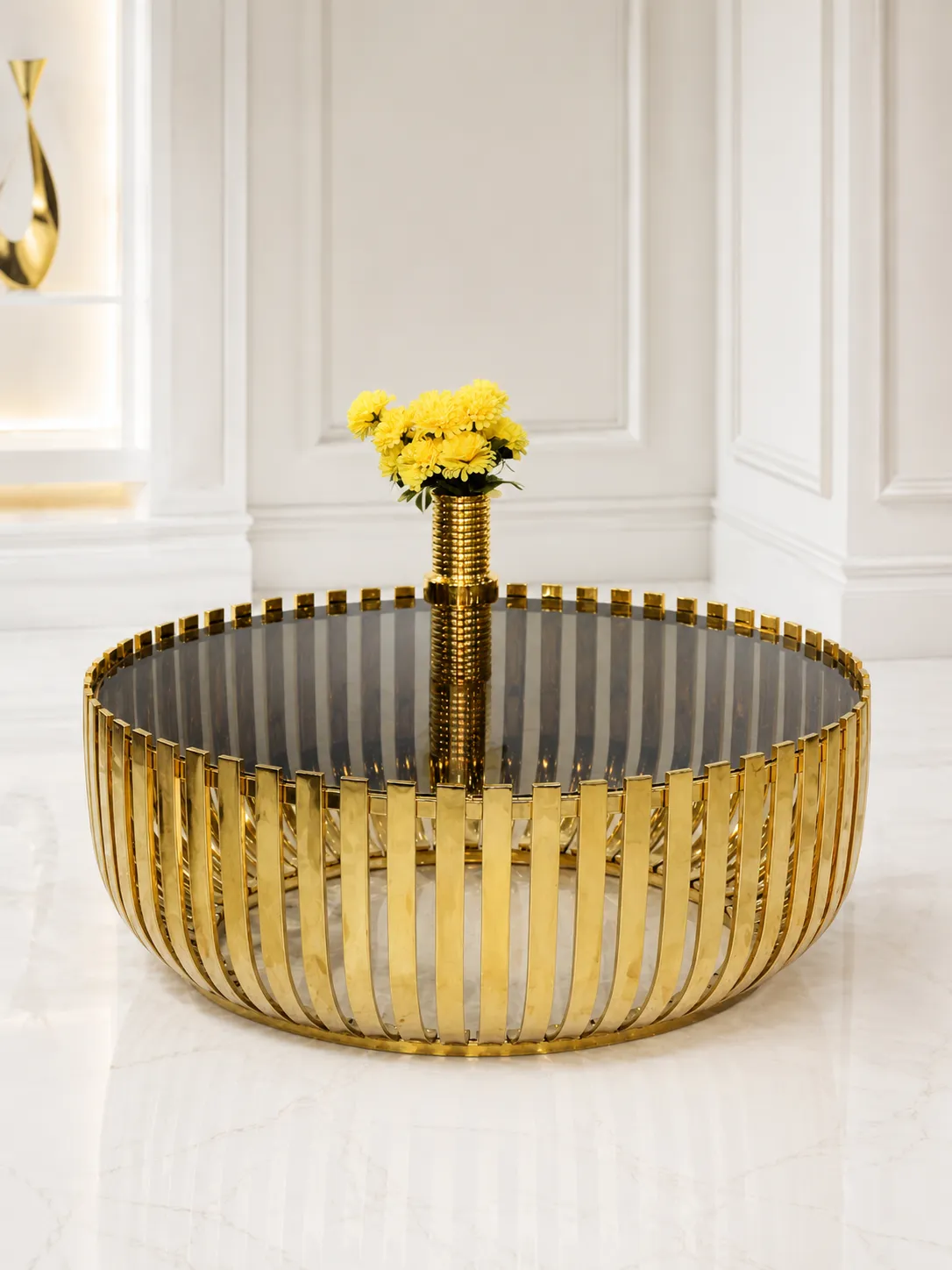 Luxury Round Smoked Glass Coffee Table – Contemporary Ribbed Gold Slat Base Center Table Luxury modern round coffee table featuring a dark smoked glass top and a drum base made of polished gold vertical metal slats, holding a matching gold flower vase.