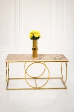 Luxury modern rectangular coffee table featuring a polished beige marble top and a geometric base made of interlocking polished gold metal rings, styled with a gold flower vase.