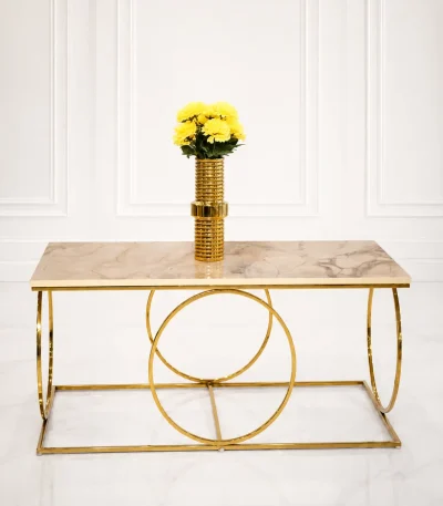 Luxury modern rectangular coffee table featuring a polished beige marble top and a geometric base made of interlocking polished gold metal rings, styled with a gold flower vase.