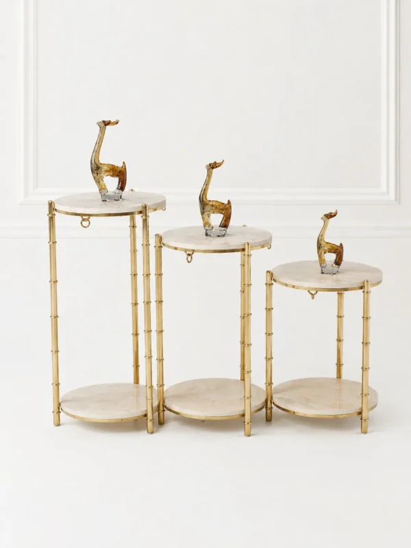 A set of three tiered round pedestal display stands with light beige marble tops and bamboo-textured gold metal frames holding giraffe figurines.