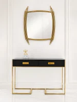 A modern high-gloss black console table with two drawers and gold legs underneath a unique curved gold-framed wall mirror against a white paneled wall.