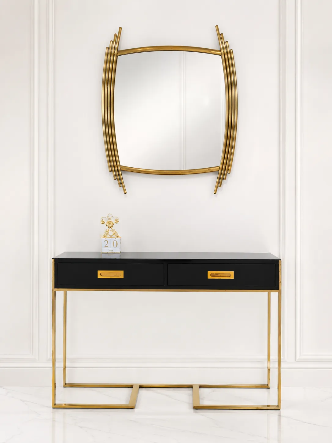Modern Luxury Black Console Table with Drawers and Matching Gold Wall Mirror Set A modern high-gloss black console table with two drawers and gold legs underneath a unique curved gold-framed wall mirror against a white paneled wall.