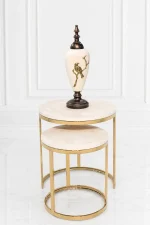 A luxury set of two round nesting side tables with light beige marble tops and polished gold circular bases supporting a decorative white and gold urn.