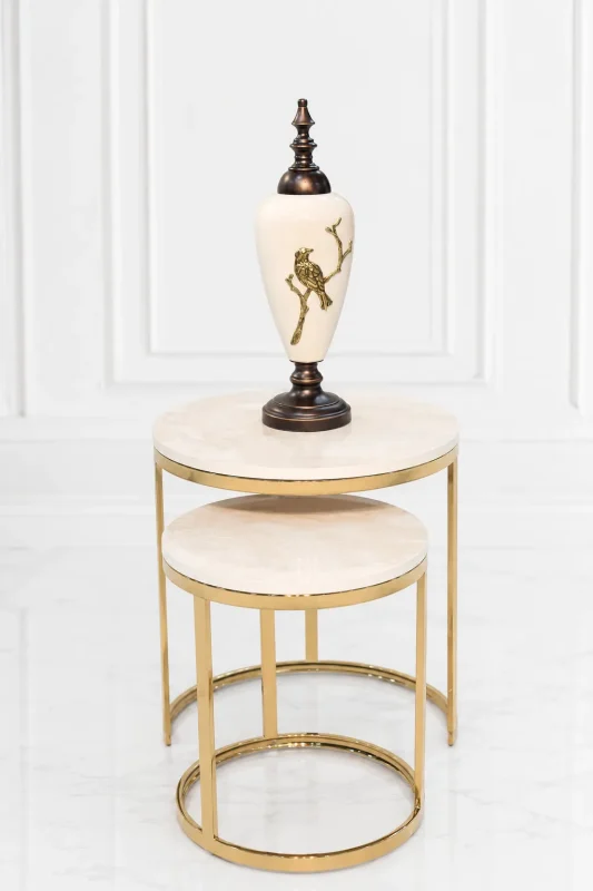 A luxury set of two round nesting side tables with light beige marble tops and polished gold circular bases supporting a decorative white and gold urn.