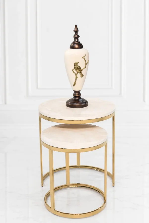 A luxury set of two round nesting side tables with light beige marble tops and polished gold circular bases supporting a decorative white and gold urn.