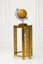 Modern luxury gold accent table featuring an intricate geometric cutout metal frame and a polished round wood top, displaying a vintage globe against a clean white wall panel background.