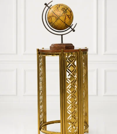 Modern luxury gold accent table featuring an intricate geometric cutout metal frame and a polished round wood top, displaying a vintage globe against a clean white wall panel background.