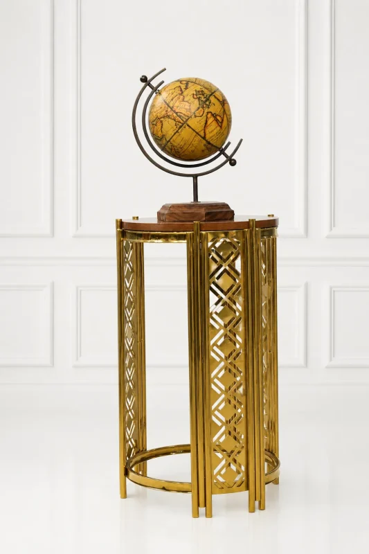 Modern luxury gold accent table featuring an intricate geometric cutout metal frame and a polished round wood top, displaying a vintage globe against a clean white wall panel background.