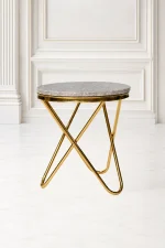 Round gold marble side table with a polished grey stone top and an architectural cross-legged gold metal base, set against a classic white wall panel interior.
