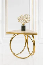Triangular cream marble side table featuring an interlocking gold ring metal base, displaying a gold coral sculpture on a dark green marble pedestal against a white wall panel background.