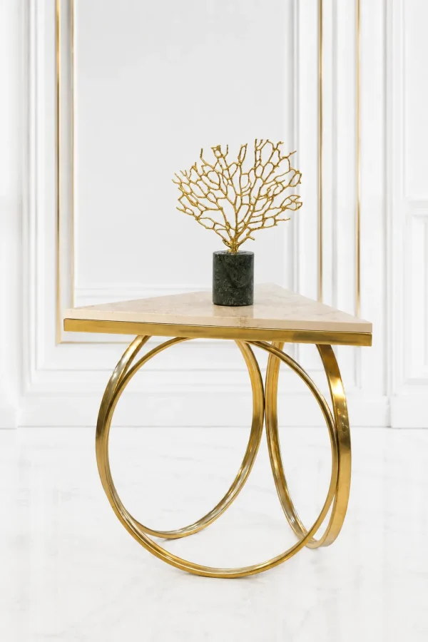 Triangular cream marble side table featuring an interlocking gold ring metal base, displaying a gold coral sculpture on a dark green marble pedestal against a white wall panel background.