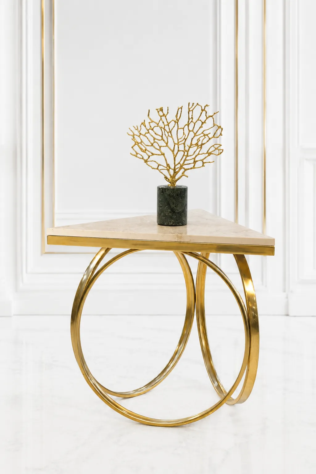 Modern Triangular Cream Marble Side Table with Interlocking Gold Hoop Base Triangular cream marble side table featuring an interlocking gold ring metal base, displaying a gold coral sculpture on a dark green marble pedestal against a white wall panel background.