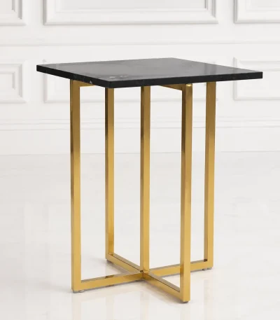 Tall square black marble side table with an architectural polished gold metal cross-base frame, positioned against a classic white wall panel background.