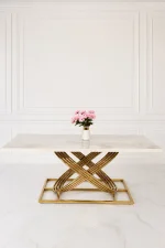 Luxury white and beige marble dining table featuring a sculptural, interlocking gold stainless steel base, set in a minimalist white paneled room.