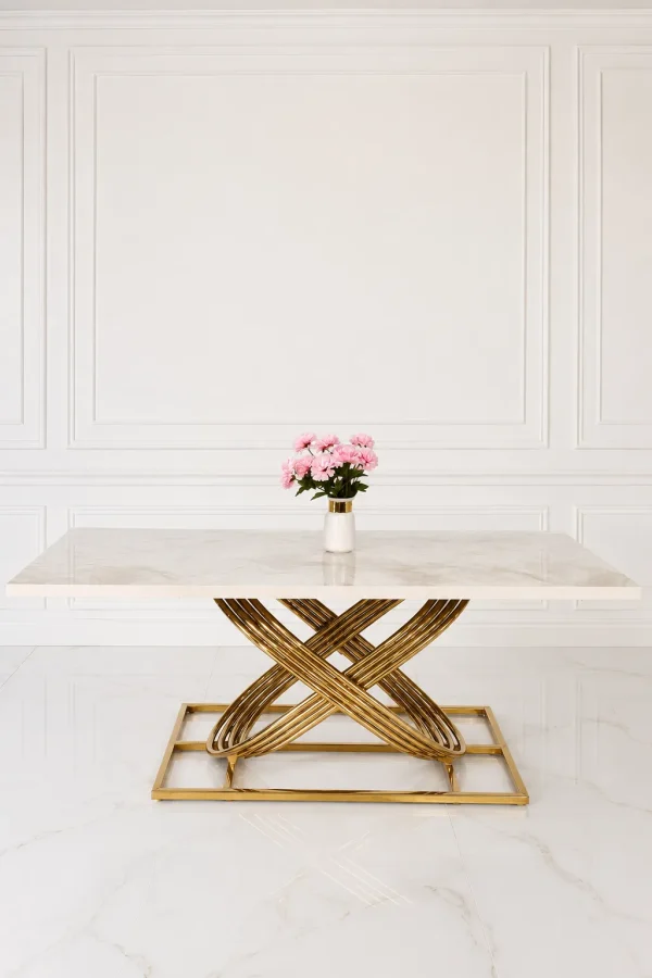 Luxury white and beige marble dining table featuring a sculptural, interlocking gold stainless steel base, set in a minimalist white paneled room.